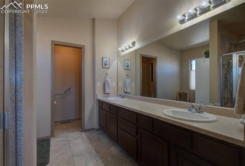 Bathroom featuring double sink, vanity with extensive cabinet space, lofted ceiling, tile floors, and an enclosed shower