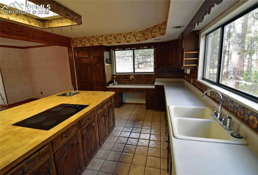 Kitchen with backsplash, black electric stovetop, light tile floors, sink, and dark brown cabinetry