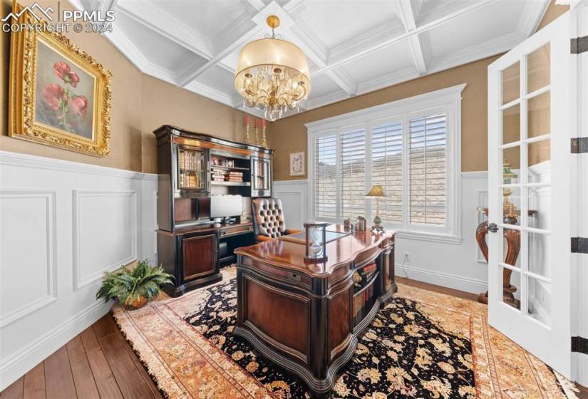 Office with coffered ceiling, white wainscoting, french doors, and large window.