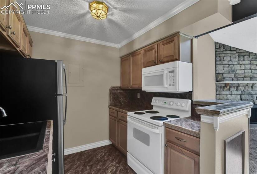 Kitchen featuring white appliances, backsplash, dark tile flooring, a textured ceiling, and sink