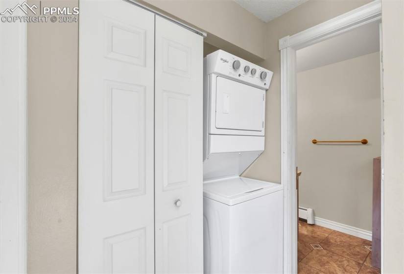 Laundry room featuring a baseboard heating unit, stacked washer and clothes dryer, and tile floors