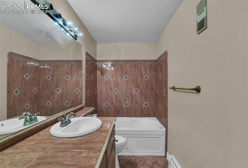 Full bathroom with large vanity, toilet, tiled shower / bath combo, and tile floors