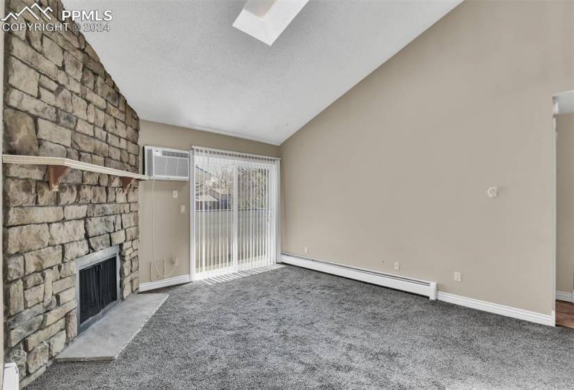 Unfurnished living room featuring dark carpet, lofted ceiling with skylight, baseboard heating, and a fireplace