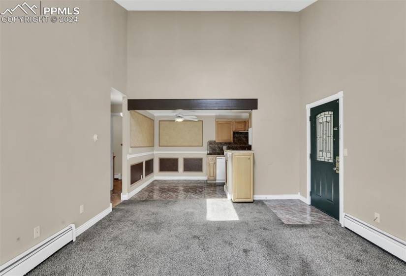 Unfurnished living room featuring a baseboard heating unit, a high ceiling, carpet floors, and ceiling fan