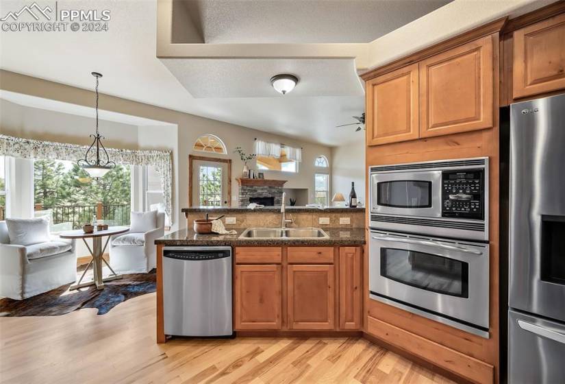 Kitchen with appliances with stainless steel finishes, ceiling fan, light hardwood / wood-style floors, sink, and a stone fireplace