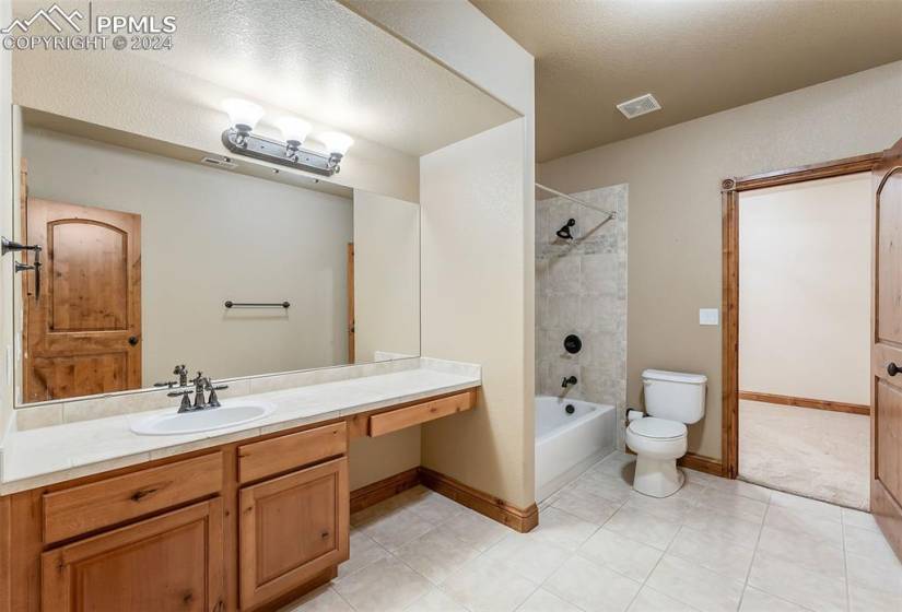 Full bathroom with tiled shower / bath combo, tile flooring, toilet, vanity, and a textured ceiling