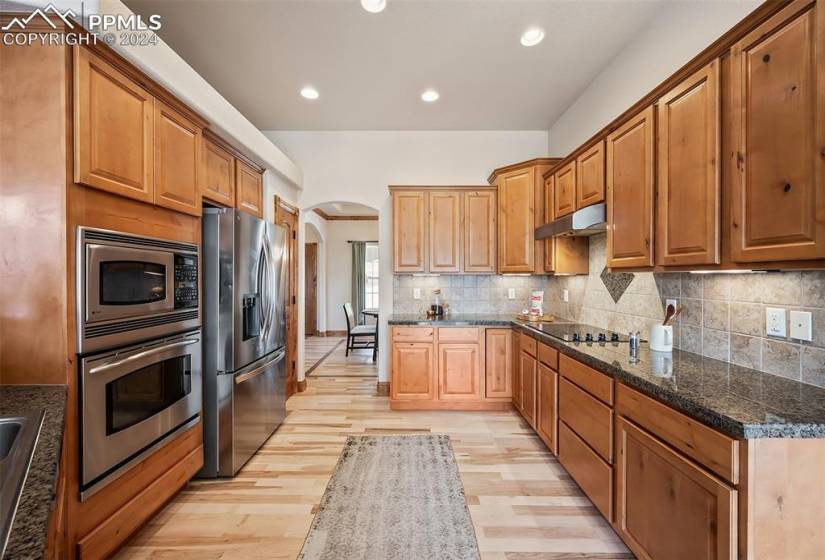 Kitchen featuring backsplash, dark stone counters, stainless steel appliances, and light hardwood / wood-style flooring