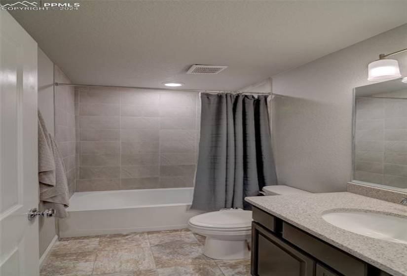 Full bathroom featuring toilet, shower / bath combo, vanity with extensive cabinet space, a textured ceiling, and tile flooring