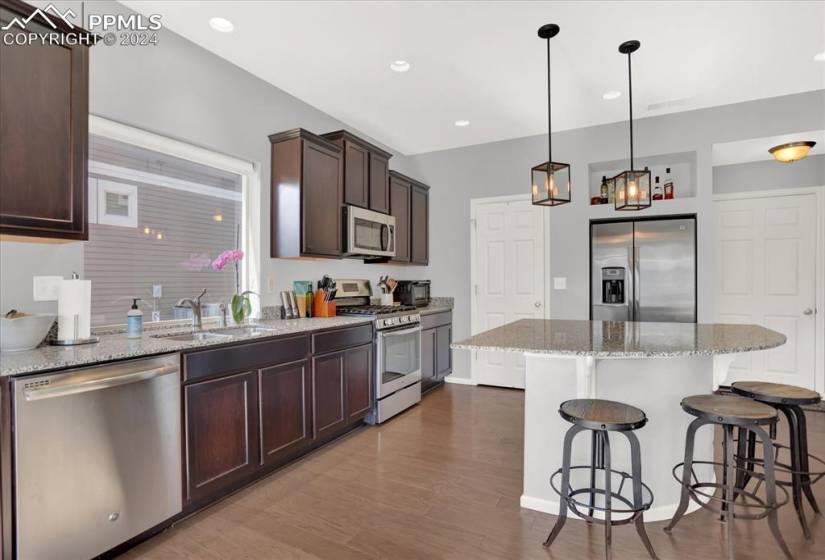 Kitchen with decorative light fixtures, stainless steel appliances, light stone counters, and LVT flooring