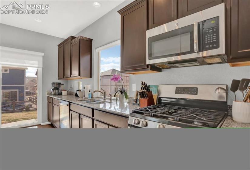 Kitchen featuring sink, light stone counters, dark brown cabinetry, and stainless steel appliances