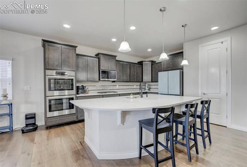 Kitchen with appliances with stainless steel finishes, dark brown cabinets, light wood-type flooring, and decorative light fixtures
