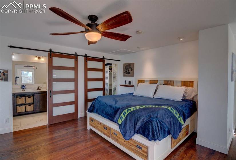 Master bedroom featuring a dual barn door, dark hardwood / wood-style flooring, ceiling fan.