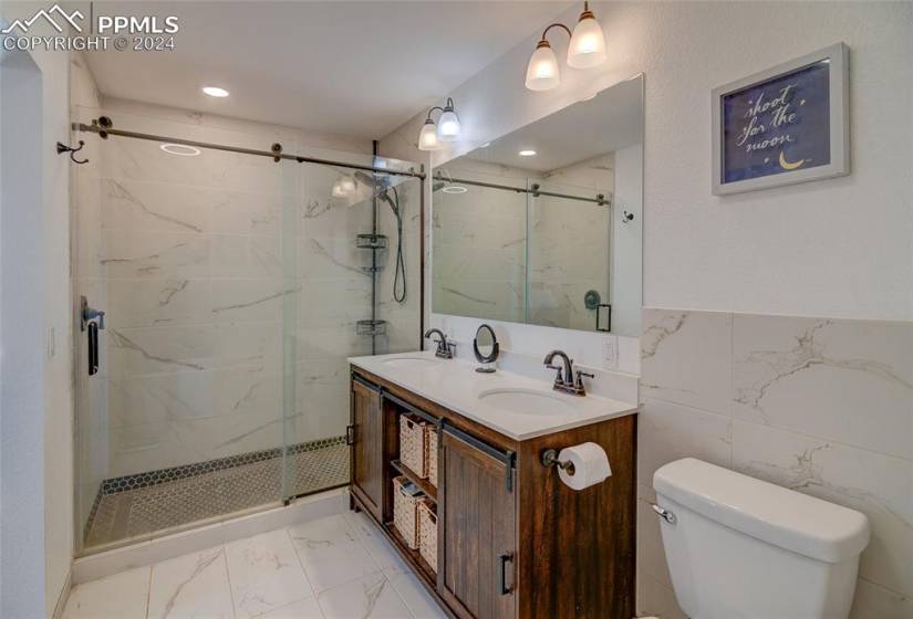 Master bathroom featuring tile walls, tile floors, toilet, a shower with shower door, and dual bowl vanity
