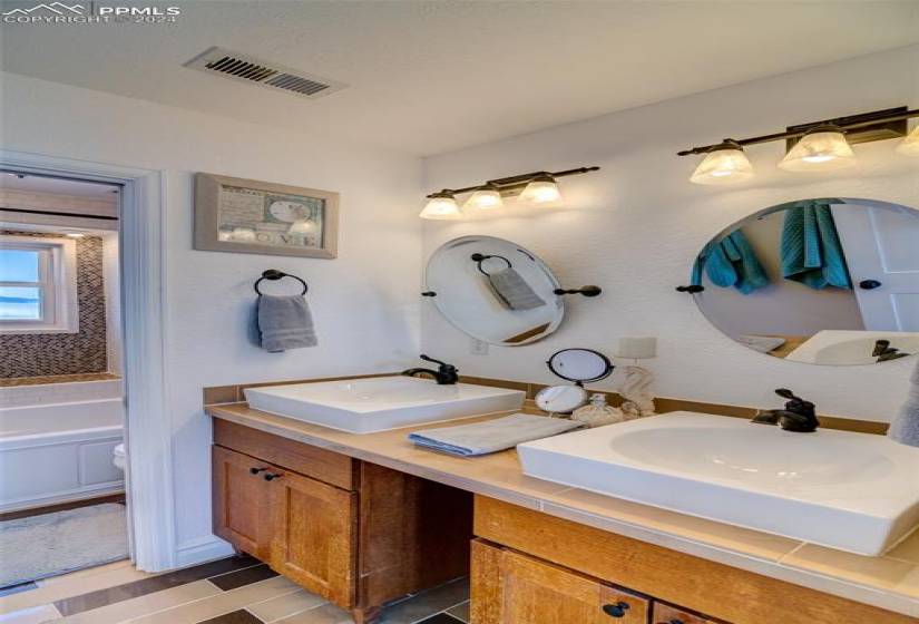 Upstairs guest bathroom with double vanity and tile floors. Separated toilet shower area.