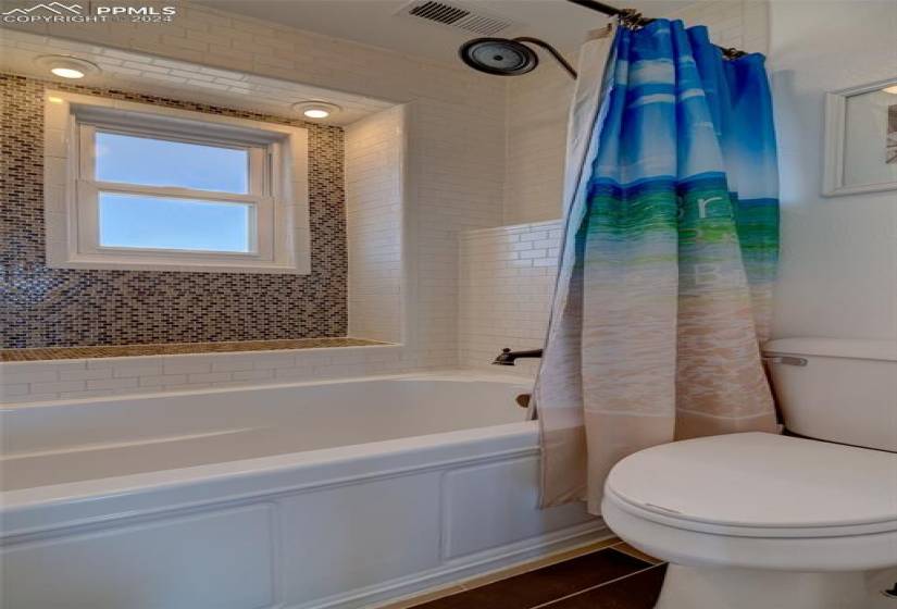Upstairs guest bathroom with tile floors, shower / bath combination with curtain, and toilet