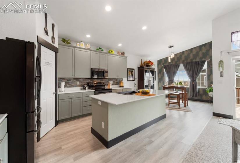 Kitchen with appliances with stainless steel finishes, a center island, backsplash, gray cabinetry, and light hardwood / wood-style flooring