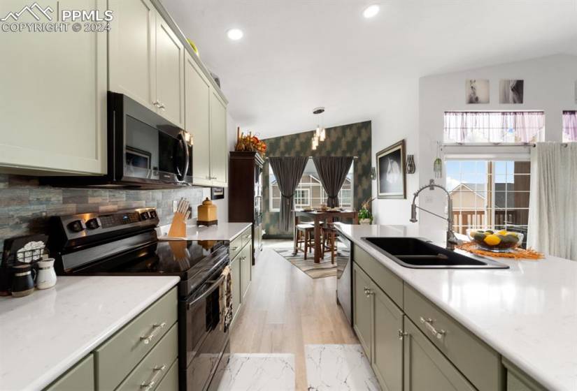 Kitchen featuring stainless steel appliances, pendant lighting, light hardwood / wood-style floors, lofted ceiling, and tasteful backsplash