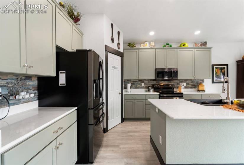 Kitchen with black fridge with ice dispenser, electric stove, light hardwood / wood-style flooring, backsplash, and sink