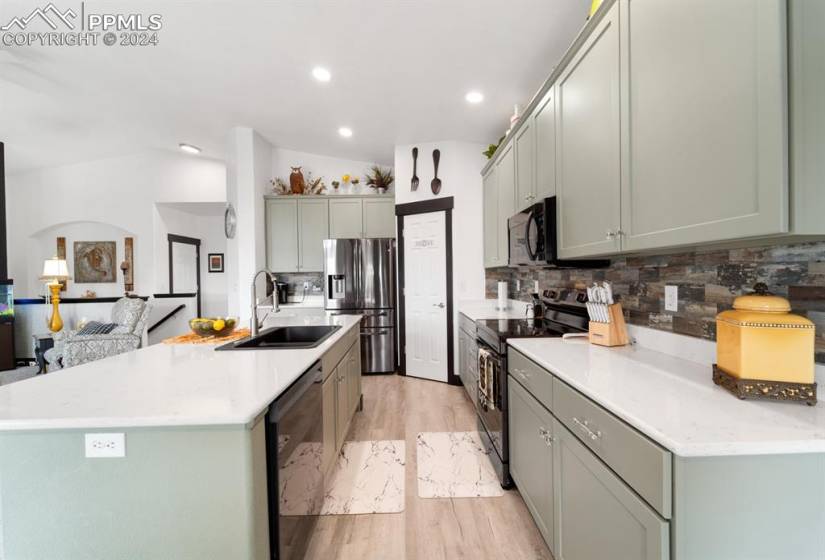 Kitchen featuring backsplash, appliances with stainless steel finishes, sink, lofted ceiling, and light wood-type flooring
