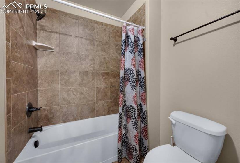 Bathroom featuring toilet and shower / bathtub combination with curtain