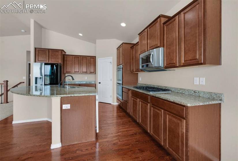 Kitchen with appliances with stainless steel finishes, dark hardwood / wood-style floors, sink, and an island with sink