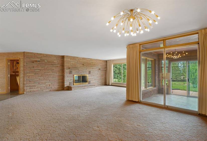 Unfurnished living room featuring an inviting chandelier, a stone fireplace, and carpet flooring