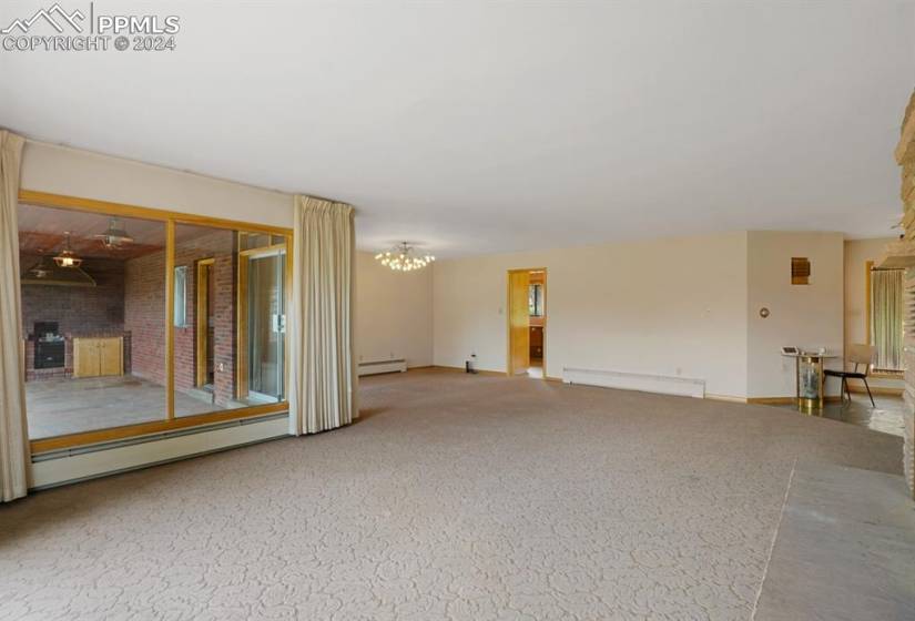 Carpeted spare room featuring a notable chandelier, baseboard heating, and brick wall