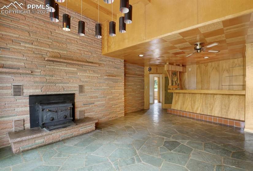Unfurnished living room featuring a fireplace, a wood stove, wood walls, and ceiling fan