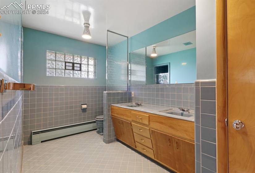 Bathroom with double sink, tile floors, large vanity, toilet, and a baseboard heating unit