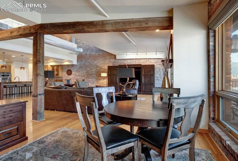 Dining space featuring beamed ceiling, original hardwood, and brick wall.