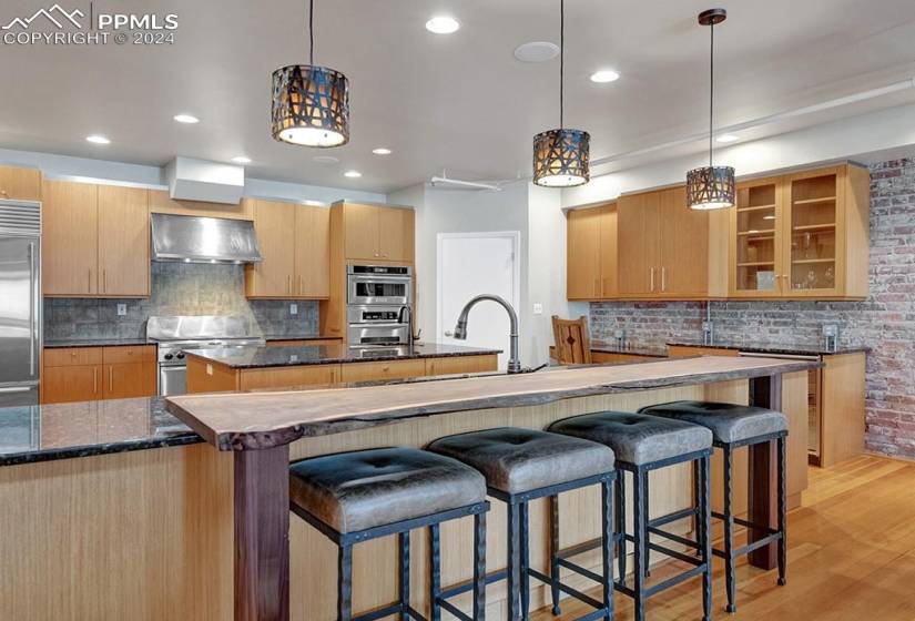 Chef's Kitchen with premium appliances, original hardwood / wall chimney range hood, brick wall, and a kitchen island with vegetable sink.