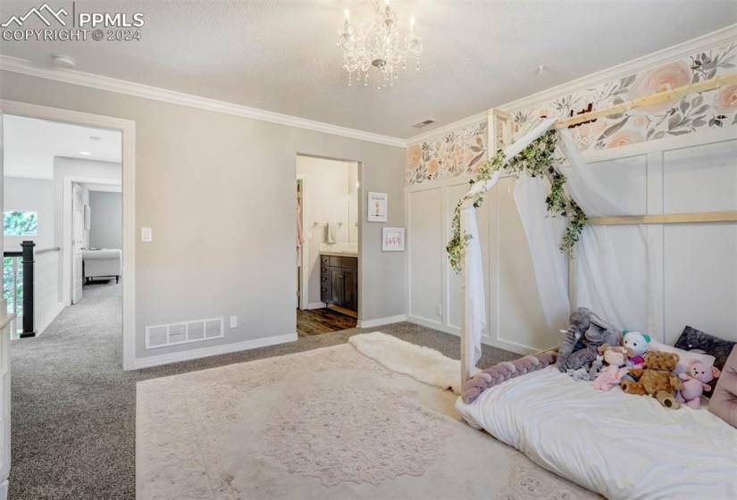 Carpeted bedroom featuring an inviting chandelier, crown molding, and connected bathroom