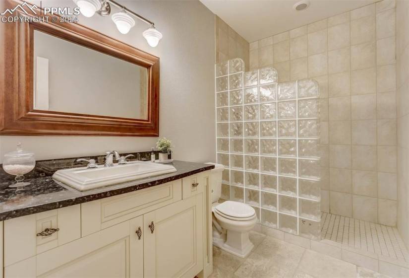 Bathroom with tile floors, toilet, vanity, and a tile shower