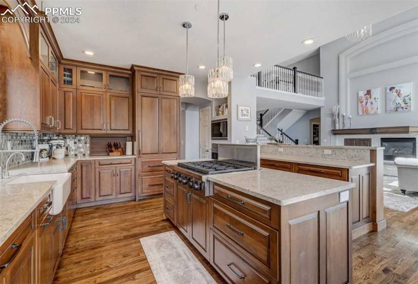 Kitchen featuring light stone counters, light hardwood / wood-style flooring, a center island, stainless steel gas stovetop, and hanging light fixtures