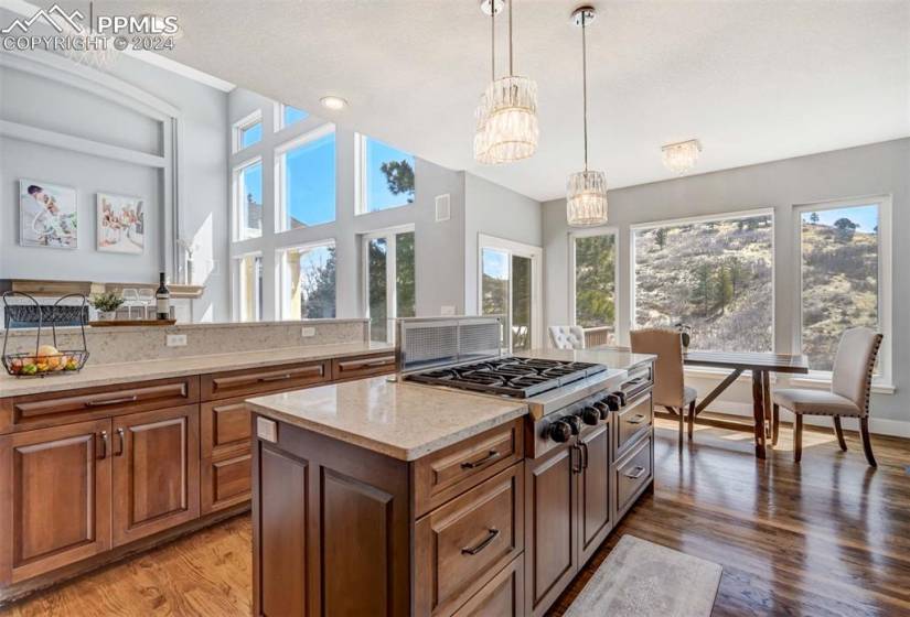 Kitchen featuring decorative light fixtures, hardwood / wood-style flooring, a kitchen island, stainless steel gas cooktop, and light stone countertops