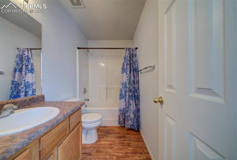Attached full bathroom featuring shower / tub combo, vanity, hardwood / wood-style flooring, and toilet