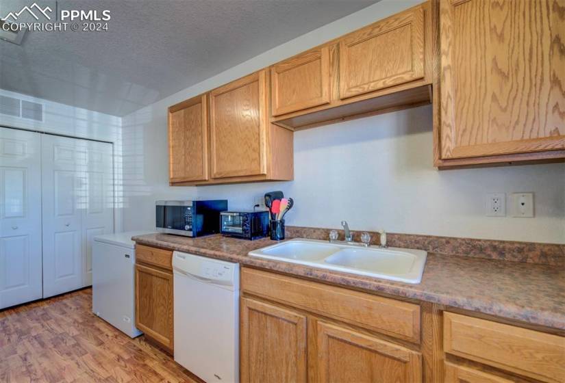 Kitchen featuring a textured ceiling, white dishwasher, sink, and light wood-type flooring