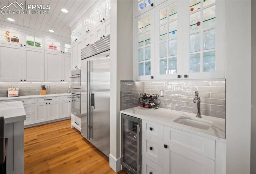 Kitchen featuring wine cooler, white cabinets, stainless steel appliances, sink, and light hardwood / wood-style floors
