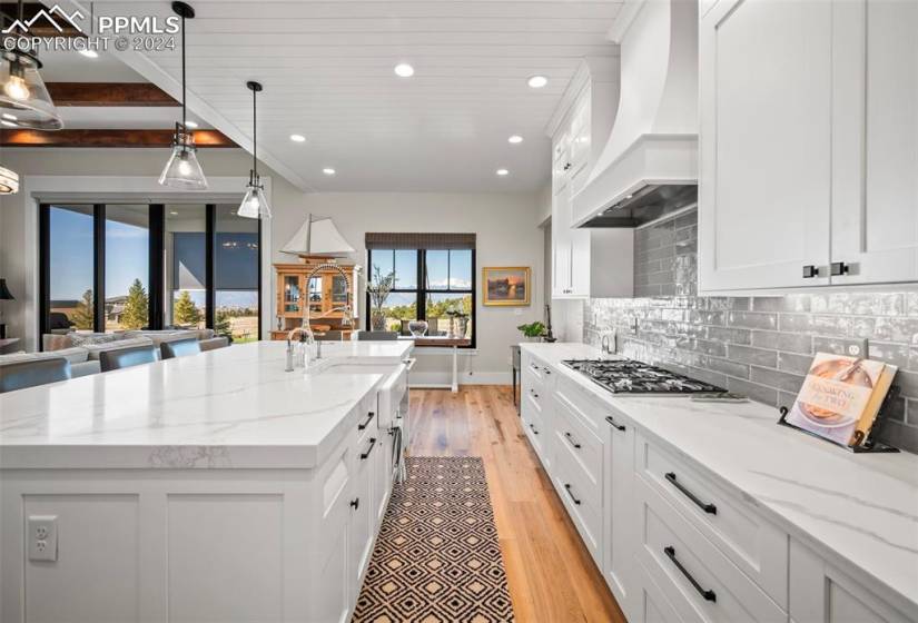 Kitchen featuring custom exhaust hood, light hardwood / wood-style floors, hanging light fixtures, beam ceiling, and stainless steel gas cooktop