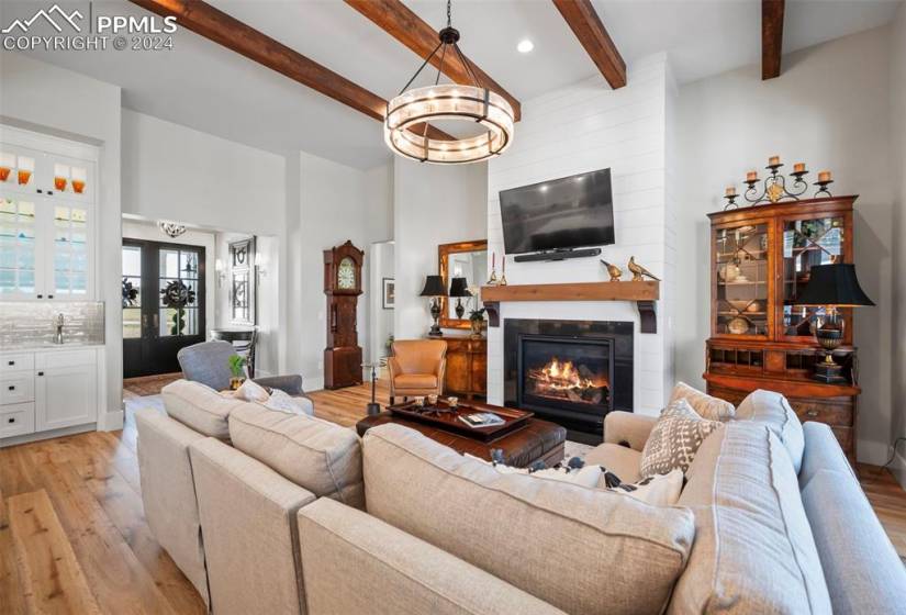 Living room with french doors, light hardwood / wood-style floors, beamed ceiling, a fireplace, and sink