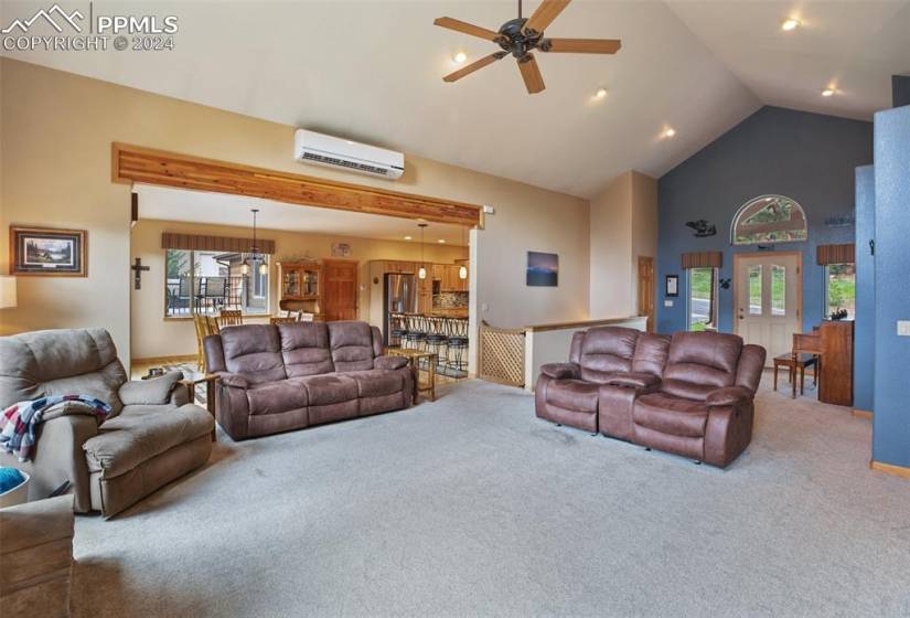 Carpeted living room featuring high vaulted ceiling, ceiling fan, and an AC wall unit