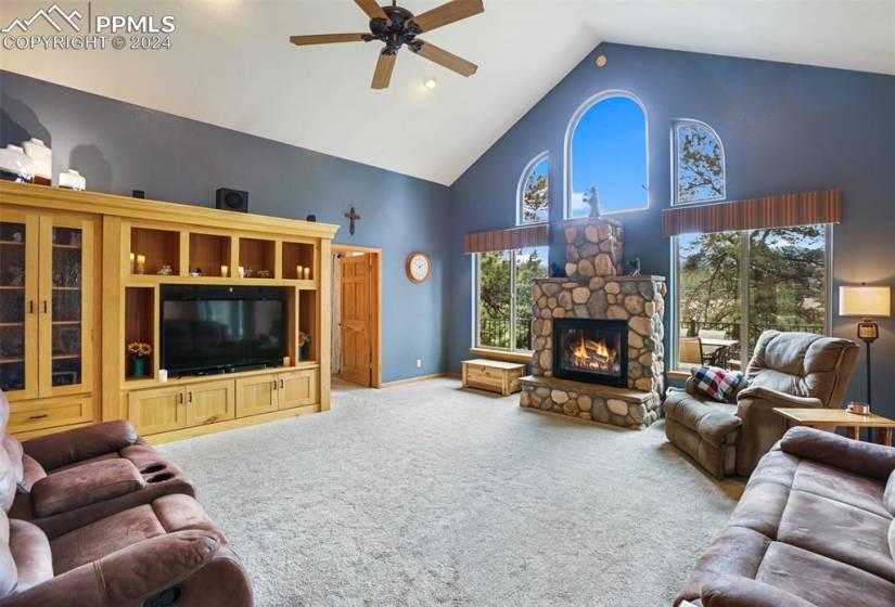 Carpeted living room with high vaulted ceiling, ceiling fan, and a stone fireplace