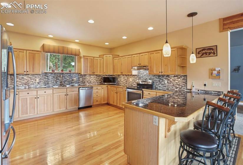 Kitchen featuring appliances with stainless steel finishes, a kitchen bar, light hardwood / wood-style floors, backsplash, and kitchen peninsula