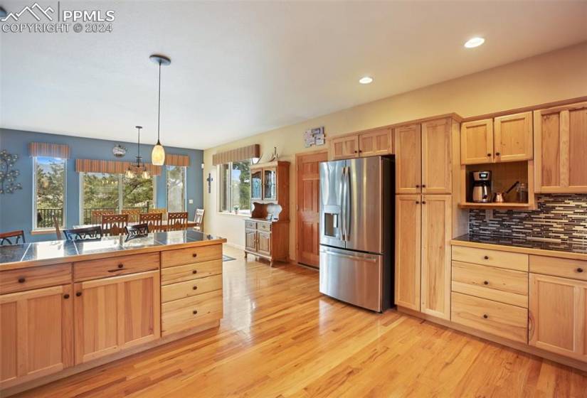 Kitchen with backsplash, pendant lighting, light wood-type flooring, and stainless steel fridge with ice dispenser