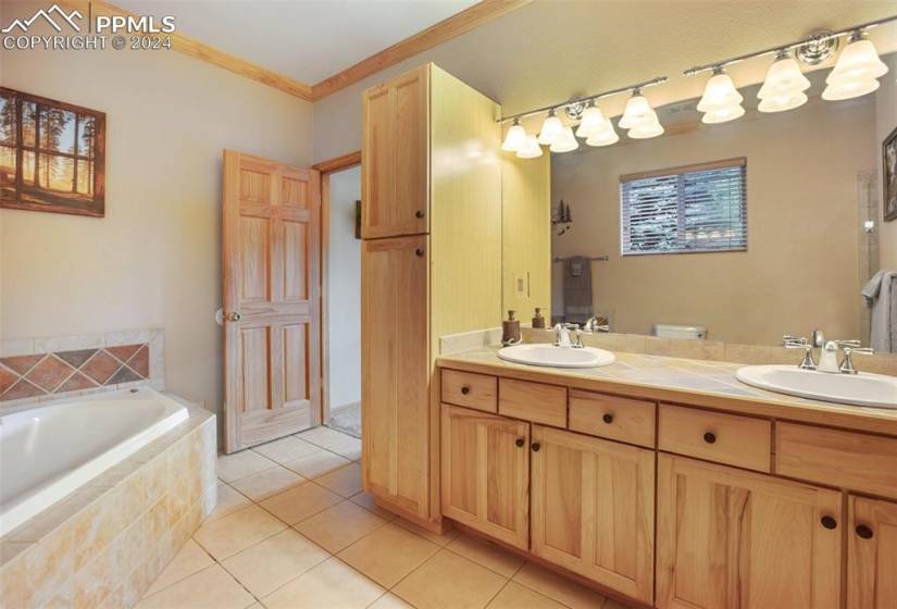 Bathroom with large vanity, a relaxing tiled bath, double sink, crown molding, and tile floors