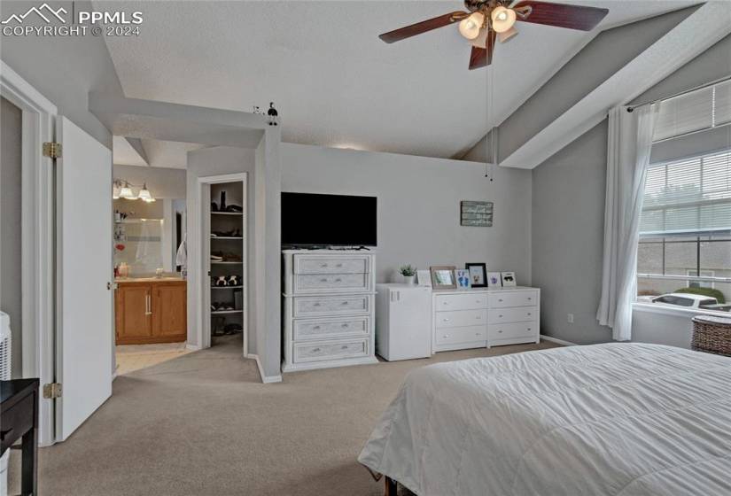 Bedroom featuring light colored carpet, a spacious closet, ensuite bathroom, ceiling fan, and vaulted ceiling