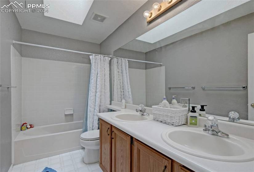 Full bathroom with dual bowl vanity, toilet, shower / tub combo with curtain, a skylight, and tile floors