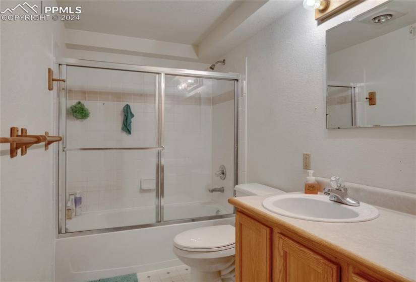 Full bathroom with tile flooring, vanity, toilet, and bath / shower combo with glass door