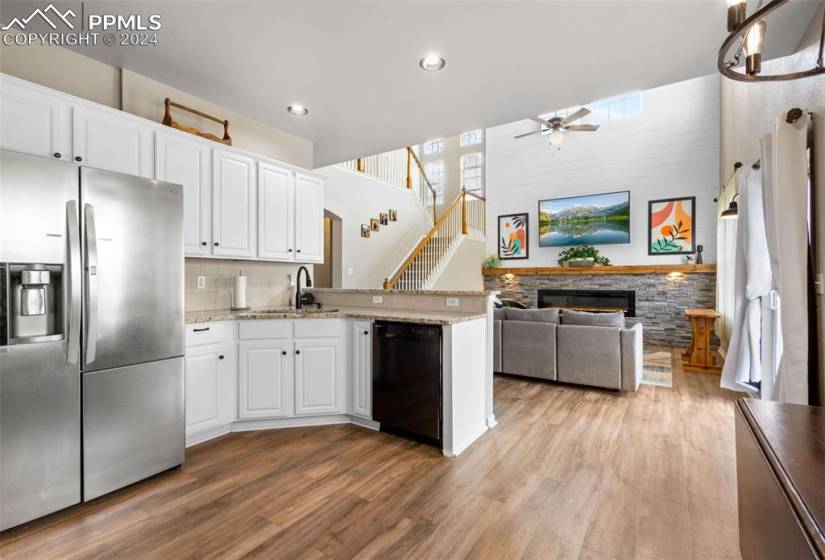 Kitchen with stainless steel fridge with ice dispenser, light hardwood / wood-style flooring, ceiling fan, black dishwasher, and a fireplace