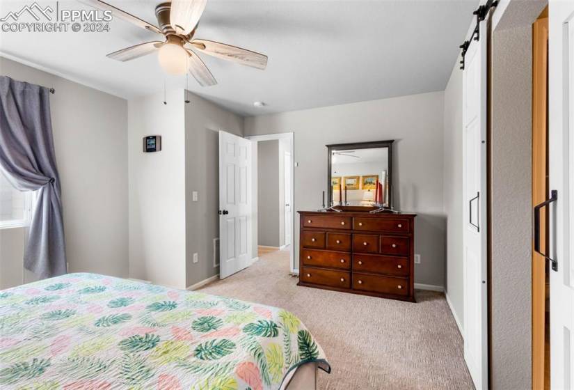 Carpeted bedroom with ceiling fan and a barn door